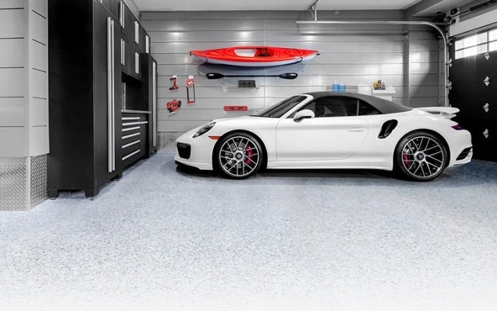 Interior of garage with concrete coated floor and tools and recreation items hanging on walls.