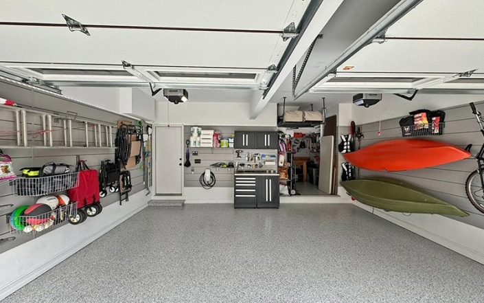 Interior of garage with concrete coated floor and tools and recreation items hanging on walls.