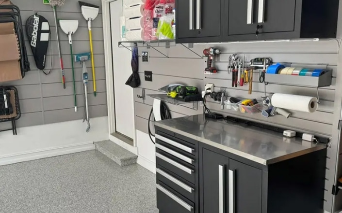 Interior of garage with concrete coated floor and tools and recreation items hanging on walls.