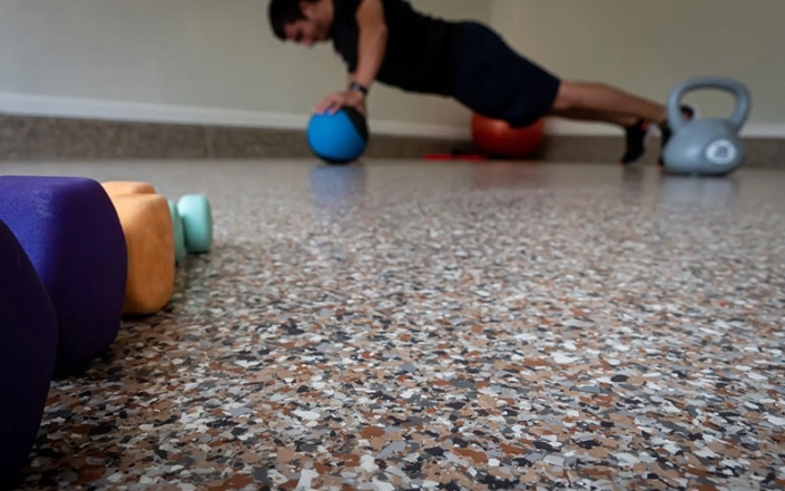 close up of flecked concrete coated basement floor with man working out in background.
