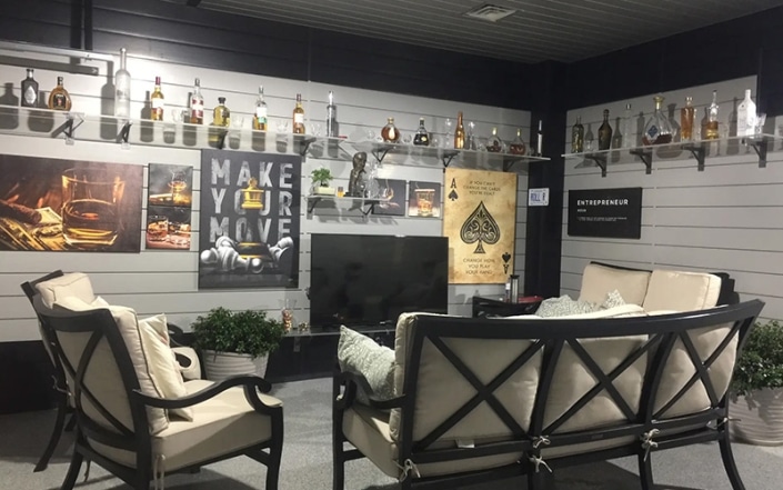 Man cave with concrete coated floor and couches facing a tv surrounded by bottles.