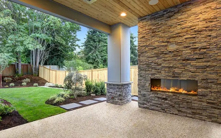Outside patio with concrete coated floor and fireplace burning.
